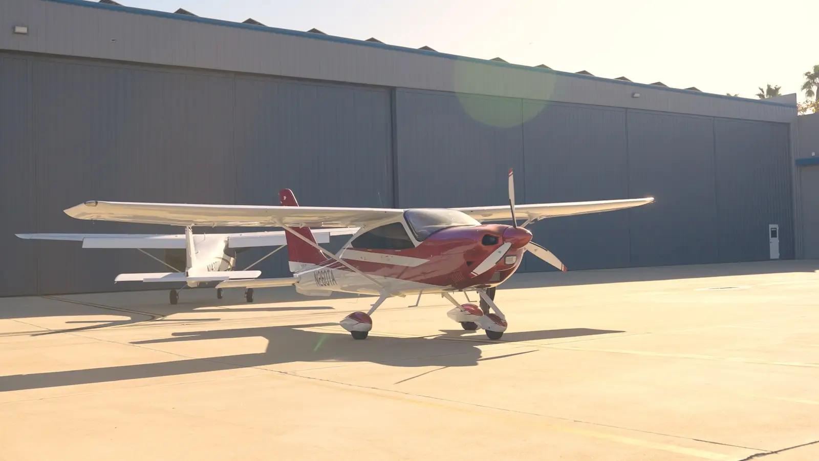 Small red and white airplane parked outside hangar.